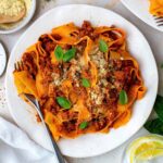 Beyond meat bolognese pasta served in a white plate and topped with fresh basil and vegan parmesan.
