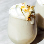 Coconut milkshake served in a glass and topped with whipped cream and coconut flakes.