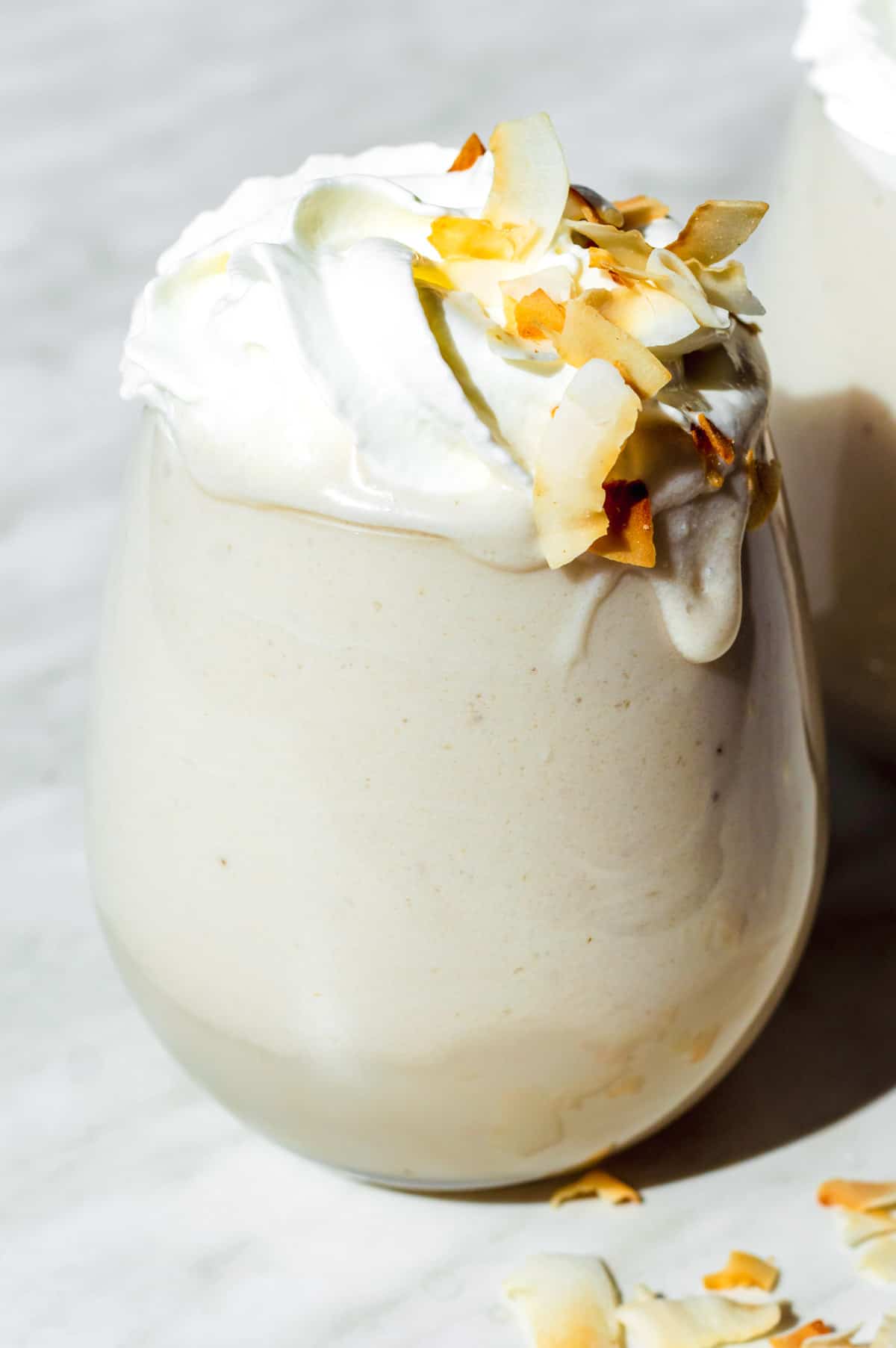 A glass filled with coconut milkshake and topped with whipped cream and coconut flakes.