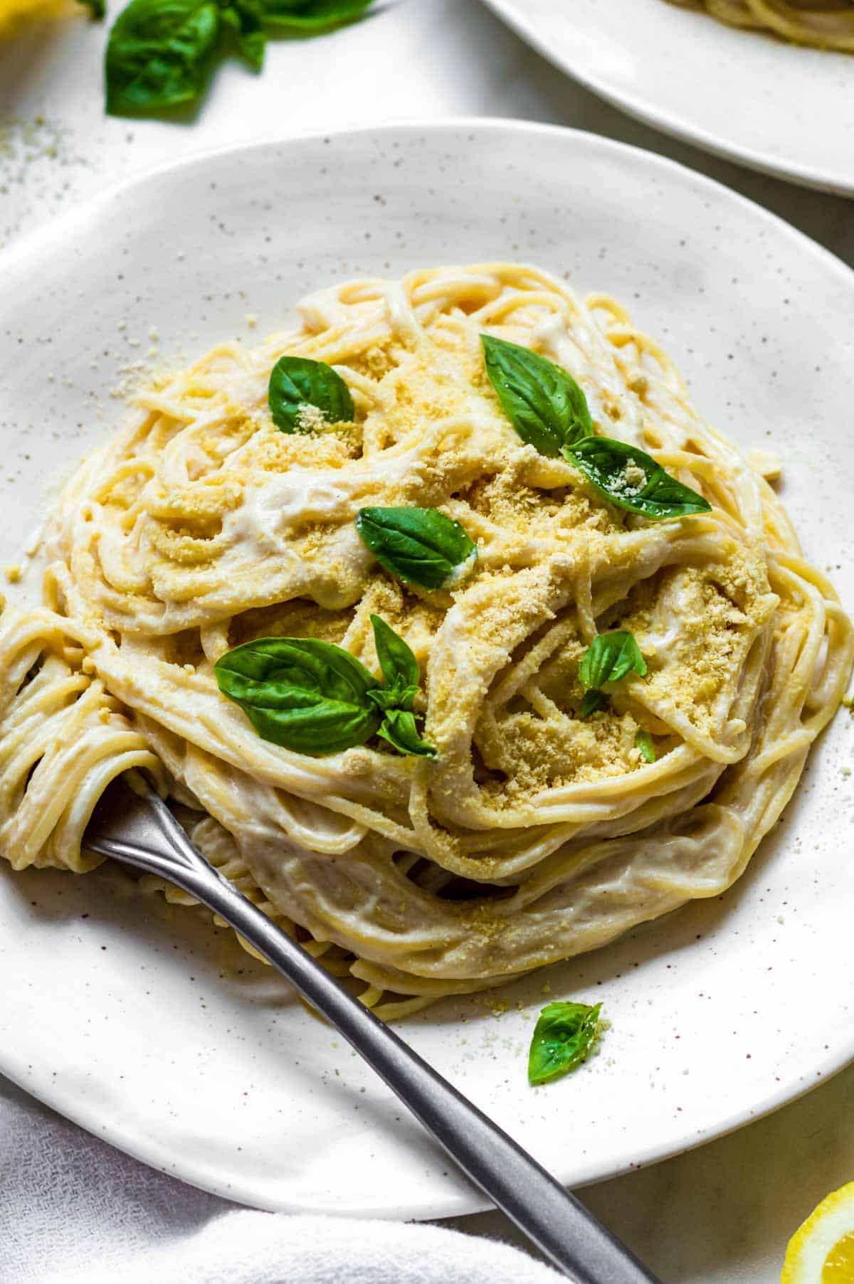 A white plate filled with tofu pasta topped with vegan parmesan cheese and basil.