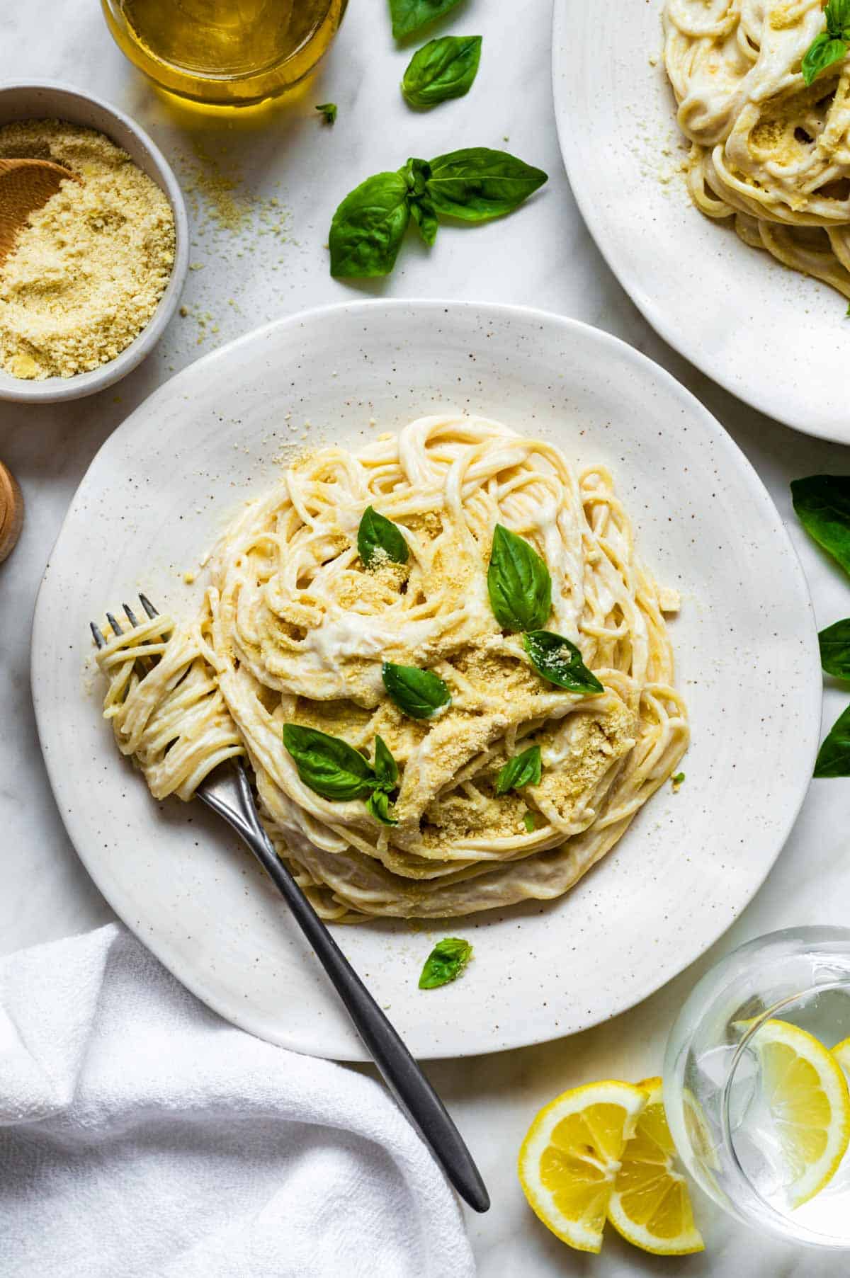 Silken tofu pasta served in a white plate and topped with vegan parmesan and fresh basil leaves.