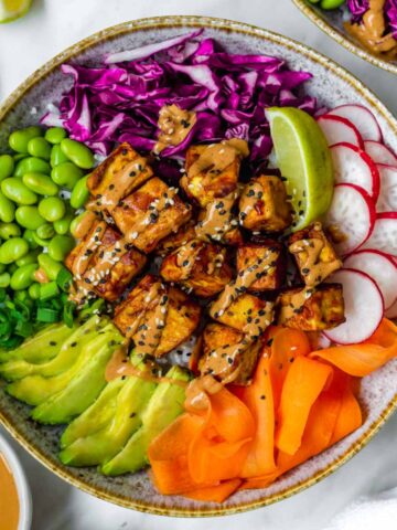 A tofu buddha bowl topped with peanut sauce and sprinkled with black and white sesame seeds.