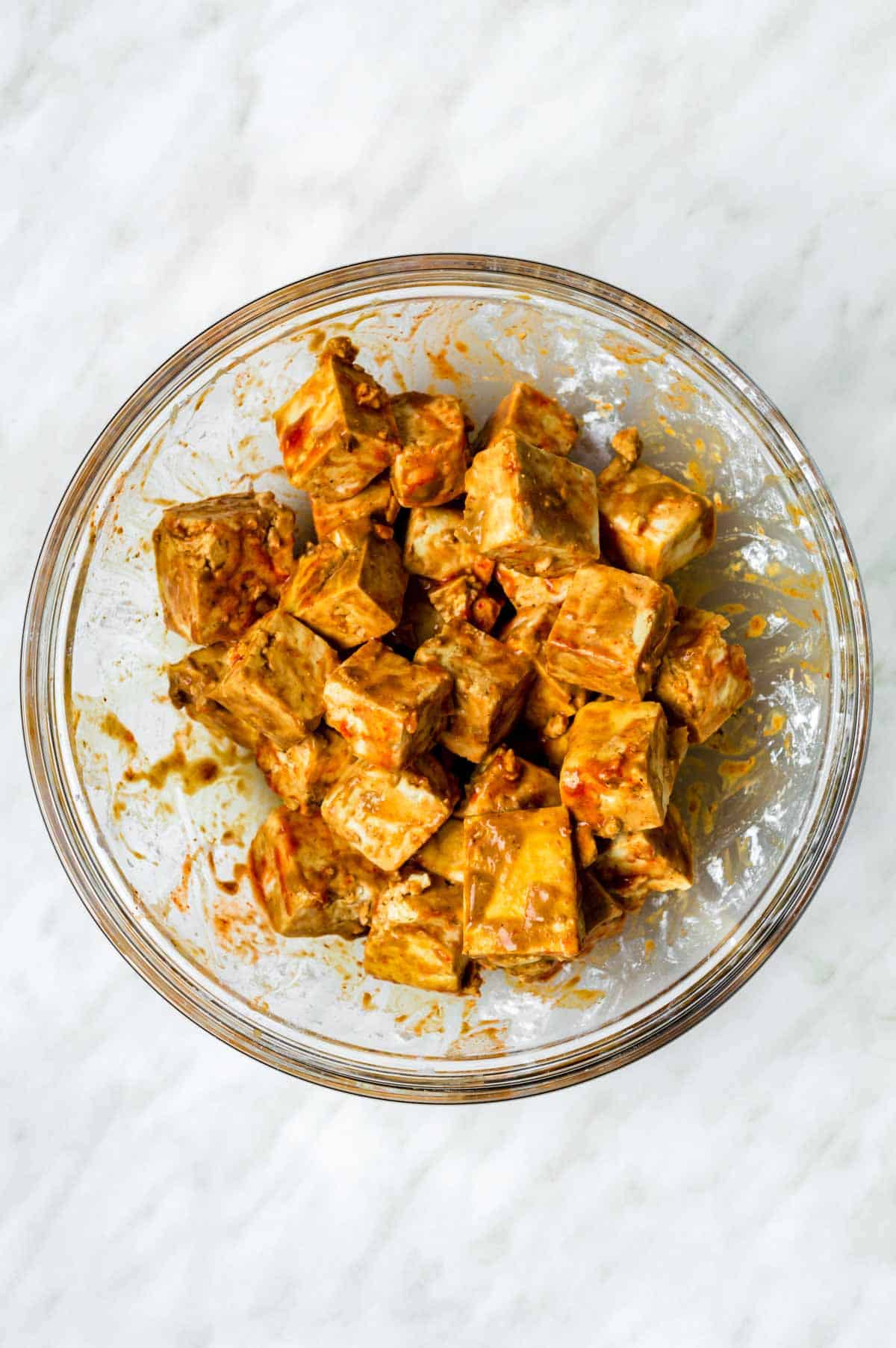 Tofu cubes coated in marinate resting in a mixing bowl.