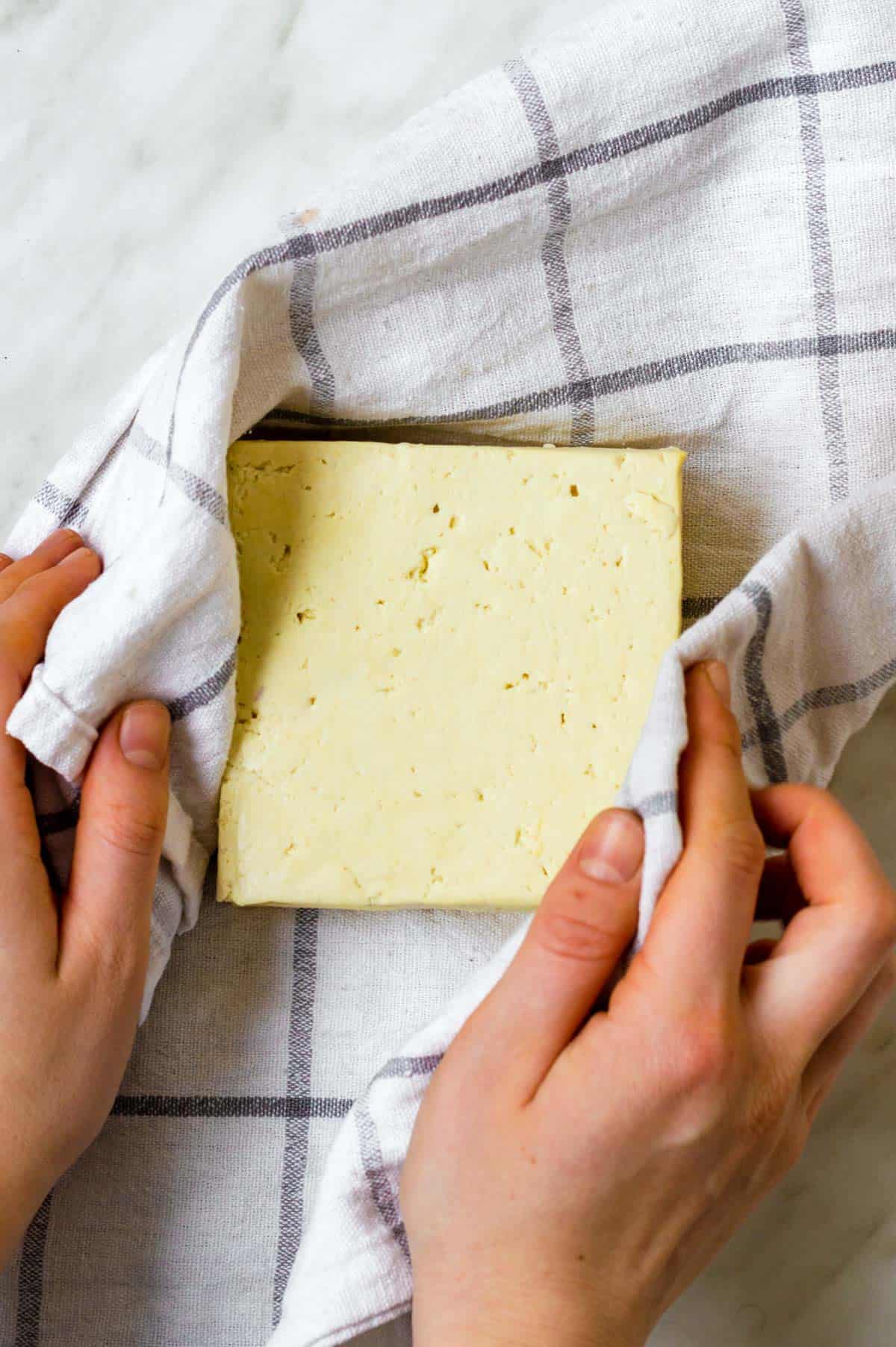 Wrapping a block of tofu in a kitchen towel to press excess liquid.