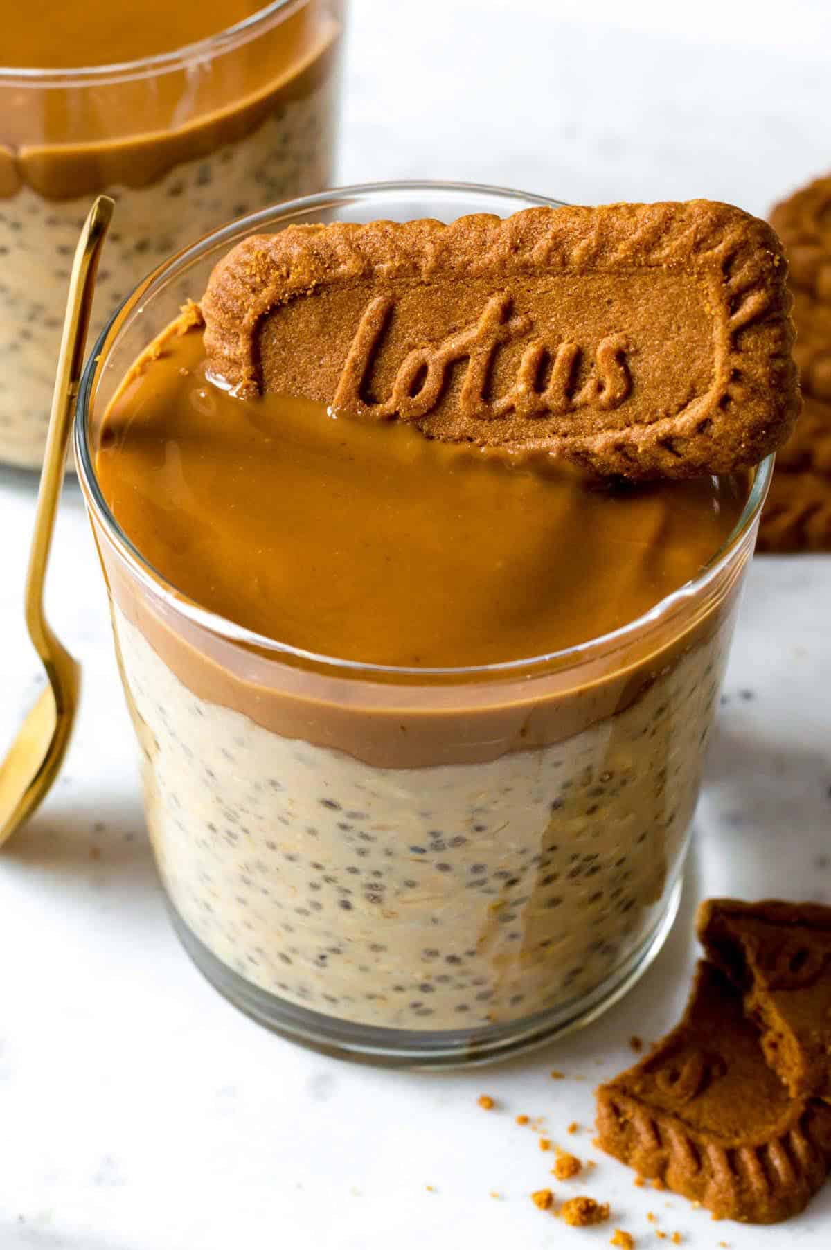 A glass cup filled with overnight oats and topped with more biscoff spred and a Lotus cookie.