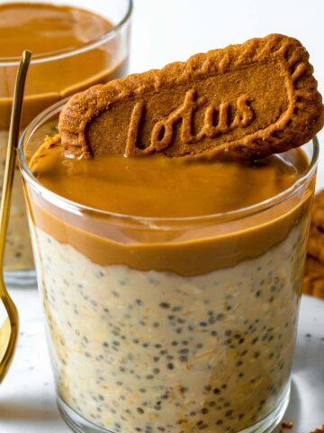 Biscoff overnight oats served in a glass cup and topped with more biscoff spred and a Lotus cookie.