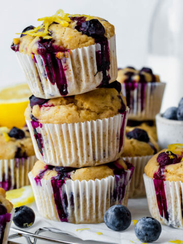 Three vegan lemon blueberry muffins stacked on top of each other and garnished with lemon zest.