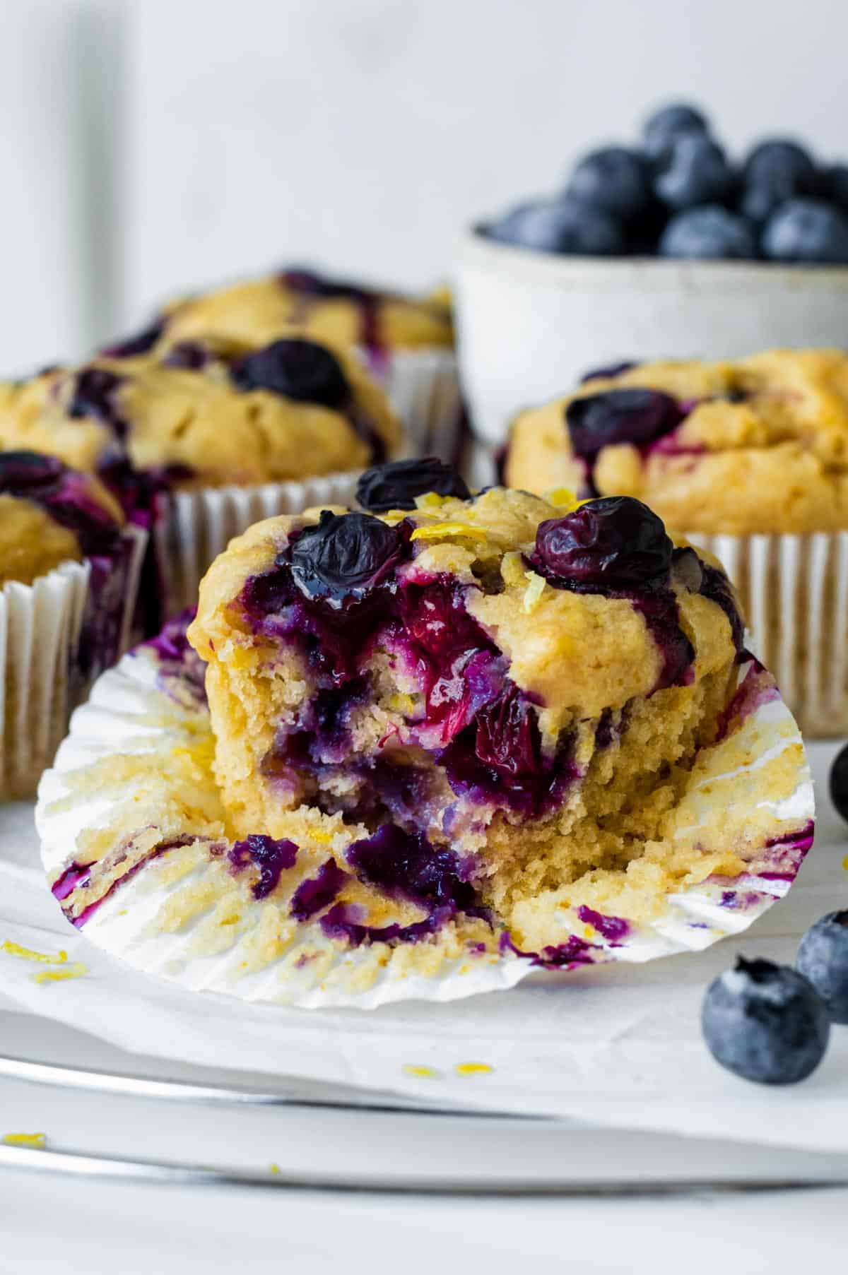 A vegan lemon blueberry muffin with a bite taken out of it, placed on a cooling rack