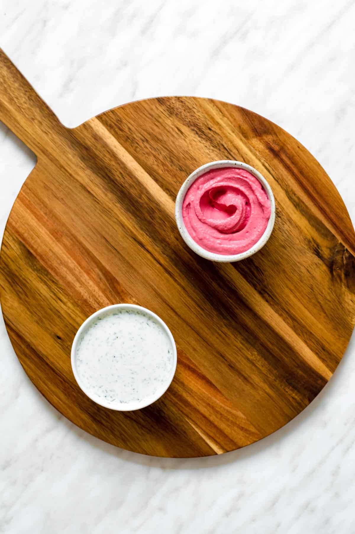 Two dips served in two white bowl, placed on a wooden board.