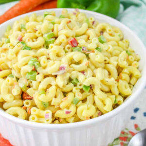 A bowl of vegan macaroni salad with carrots, green pepper, and celery in the background.