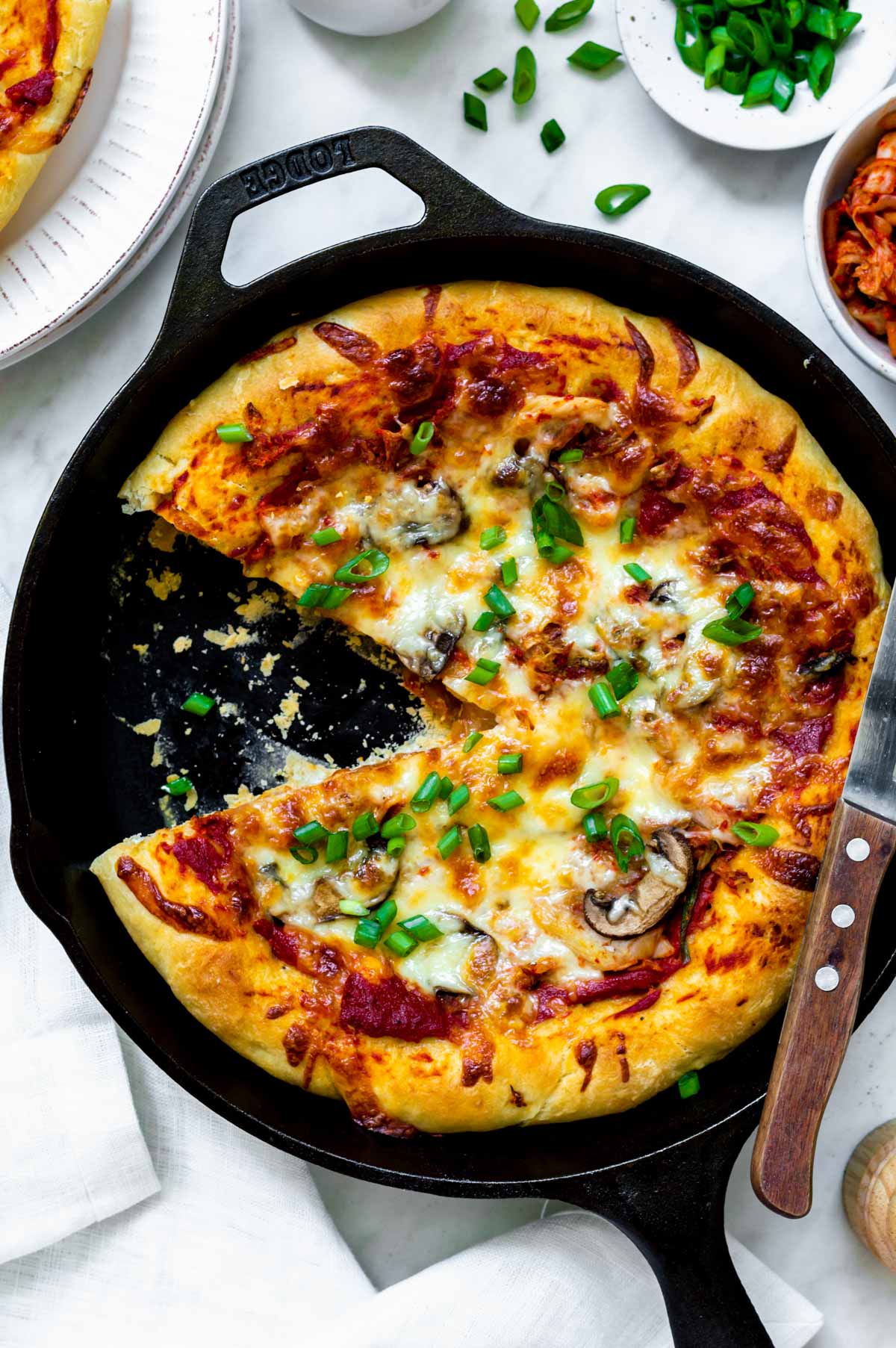 Kimchi pizza on a cast iron skillet with a single piece sliced off.