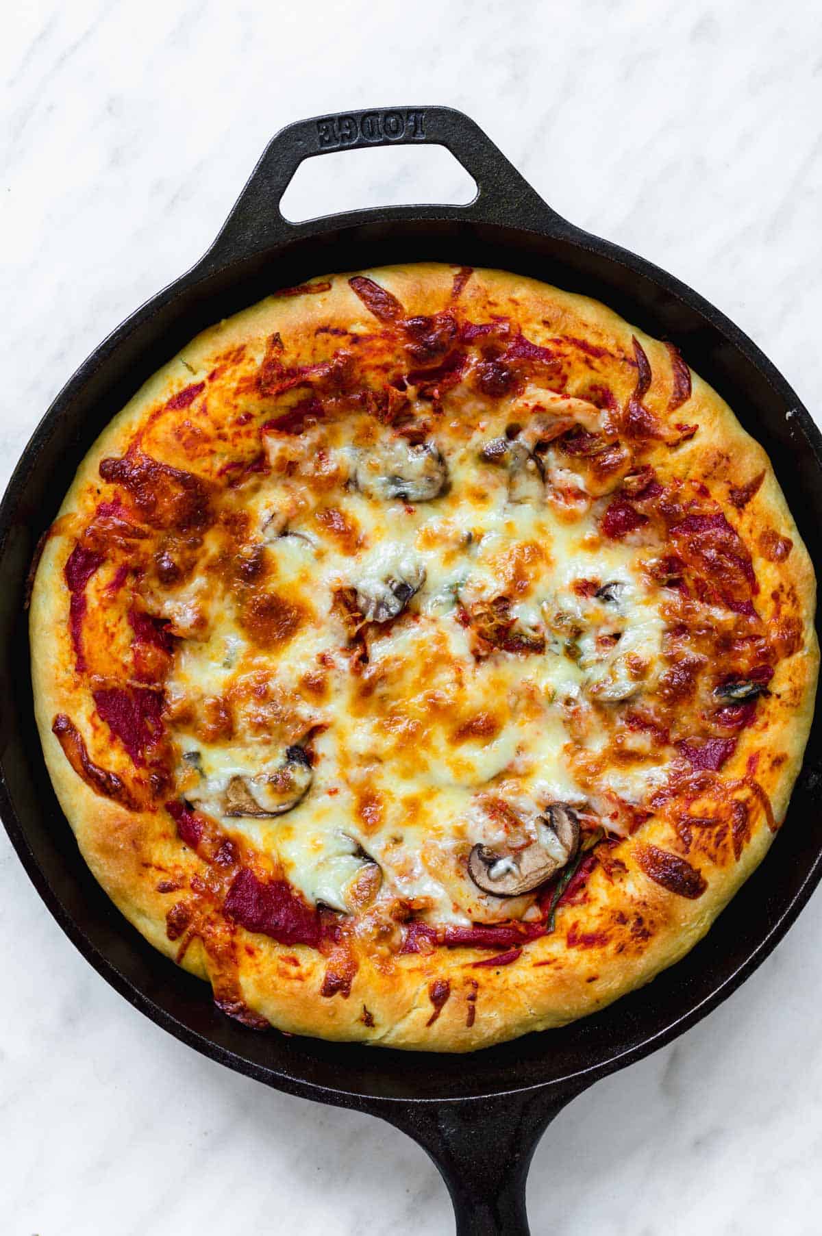 Kimchi pizza in a round iron skillet on a white background.