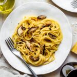 Miso spaghetti pasta served on a white plate and topped with fried shiitake mushrooms and crushed nori sheets.
