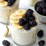 Overnight oats without chia seeds served in two glass cups and topped with sliced banana and blackberries.