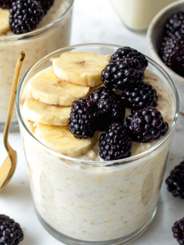 Overnight oats without chia seeds served in two glass cups and topped with sliced banana and blackberries.
