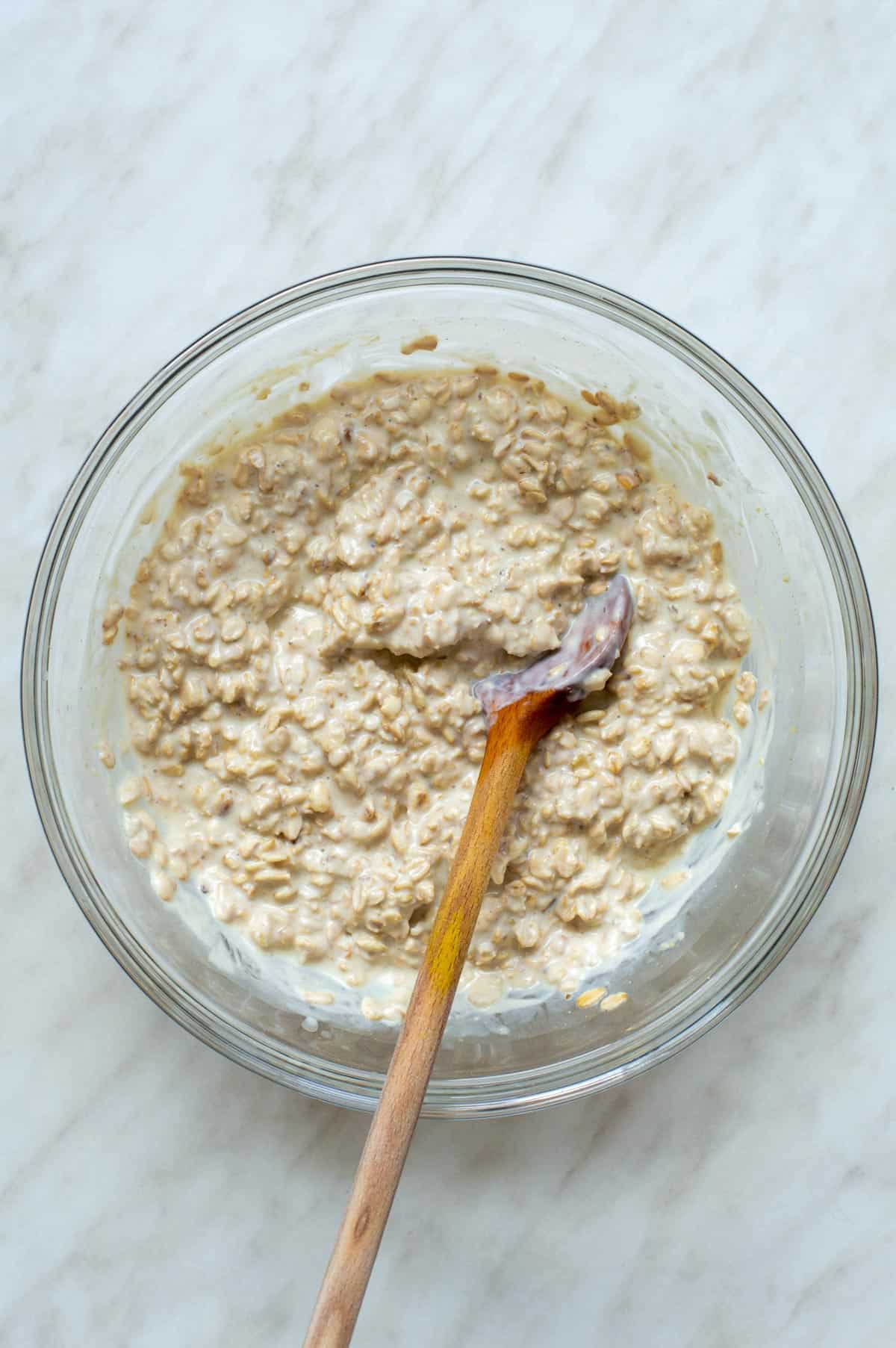 Overnight oats soaking in a large bowl with a wooden spoon in it.