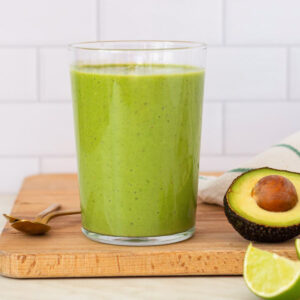 A tall glass filled with green smoothie, placed on a wooden cutting board.
