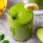 A glass of avocado fruit smoothie on a table with fresh avocado and other ingredients around it.