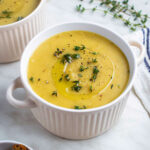 Potato leek soup served in a white bowl and topped with fresh thyme.