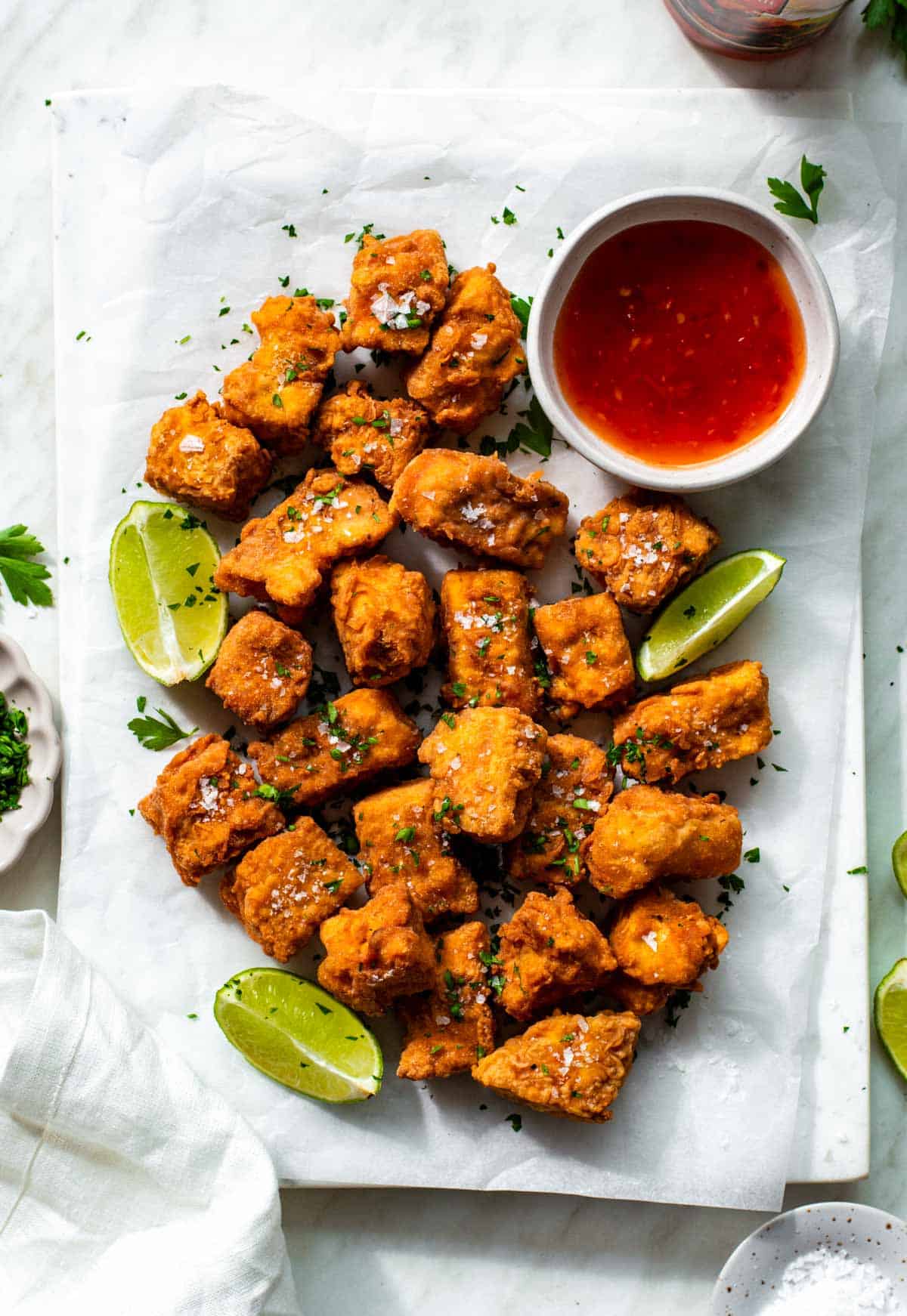 Deep fried battered tofu nuggets resting on a piece of parchment paper. They're topped with sea salt and parsley.