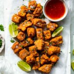 Deep fried battered tofu nuggets resting on a piece of parchment paper. They're topped with sea salt and parsley.