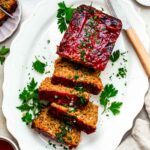 Sliced Beyond Meat meatloaf in a large white plate. The meatloaf is topped with chopped parsley.