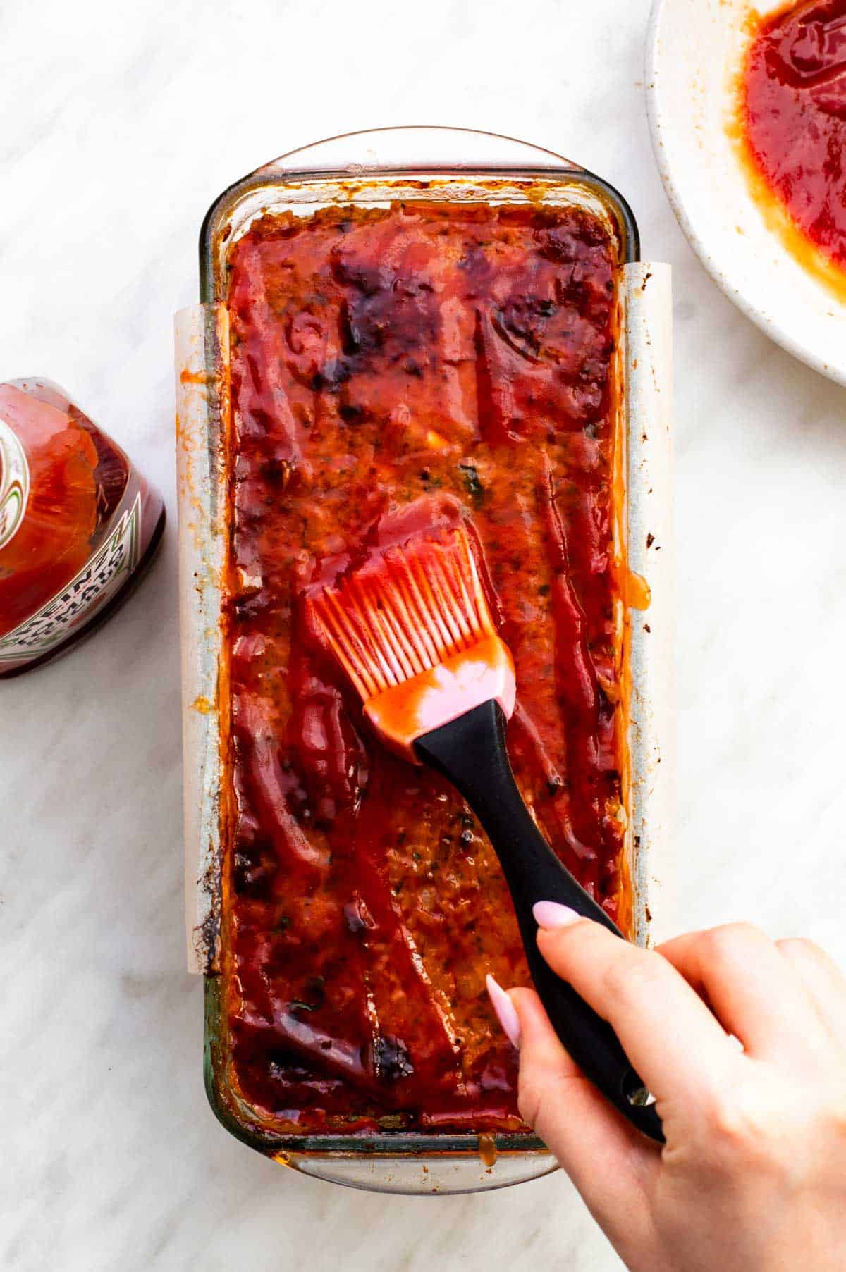 Brushing meatloaf with ketchup glaze using a pink pastry brush.