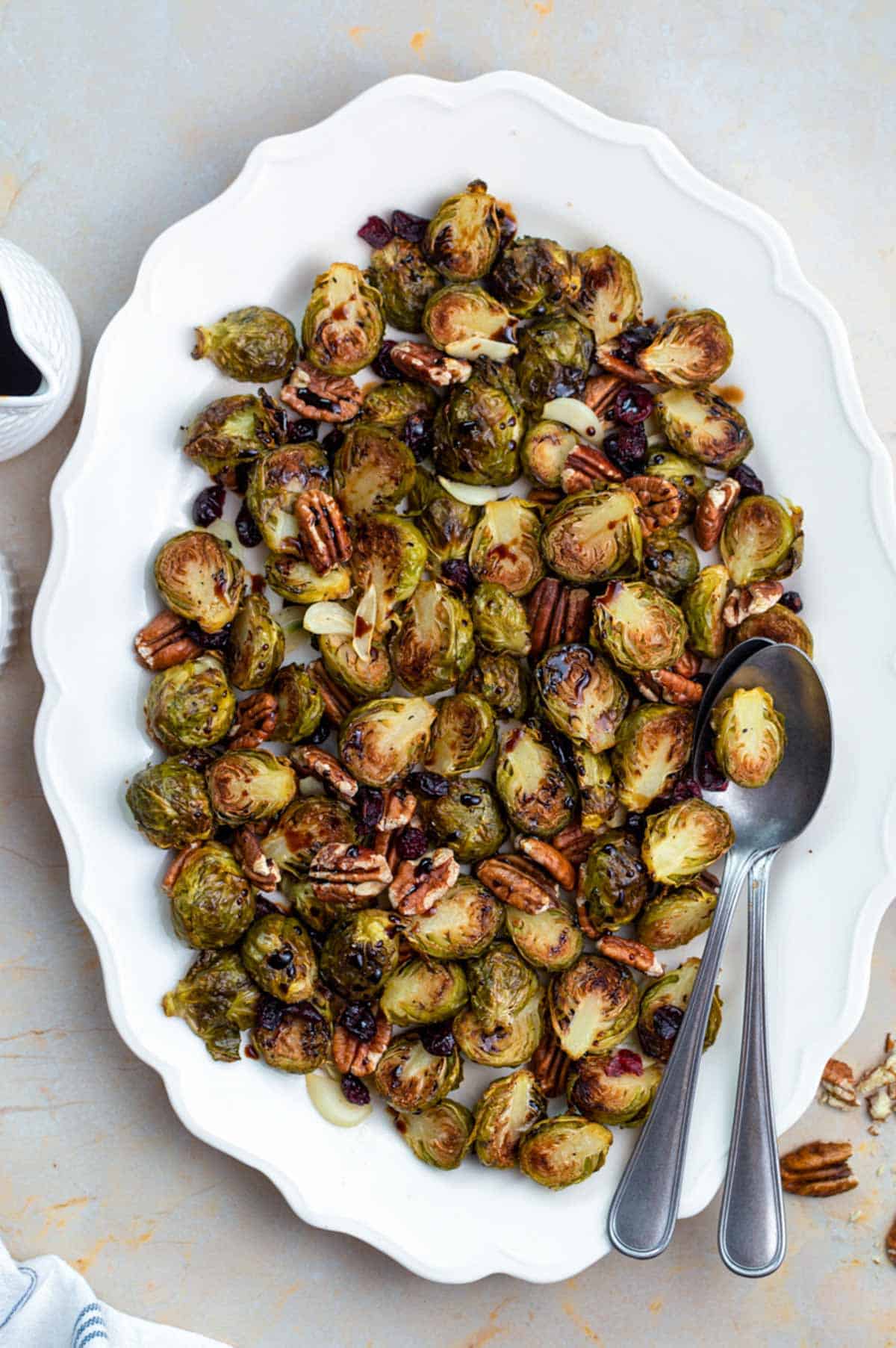 Crispy Brussels sprout served on a white plate and topped with pecans, garlic, and dried cranberries.