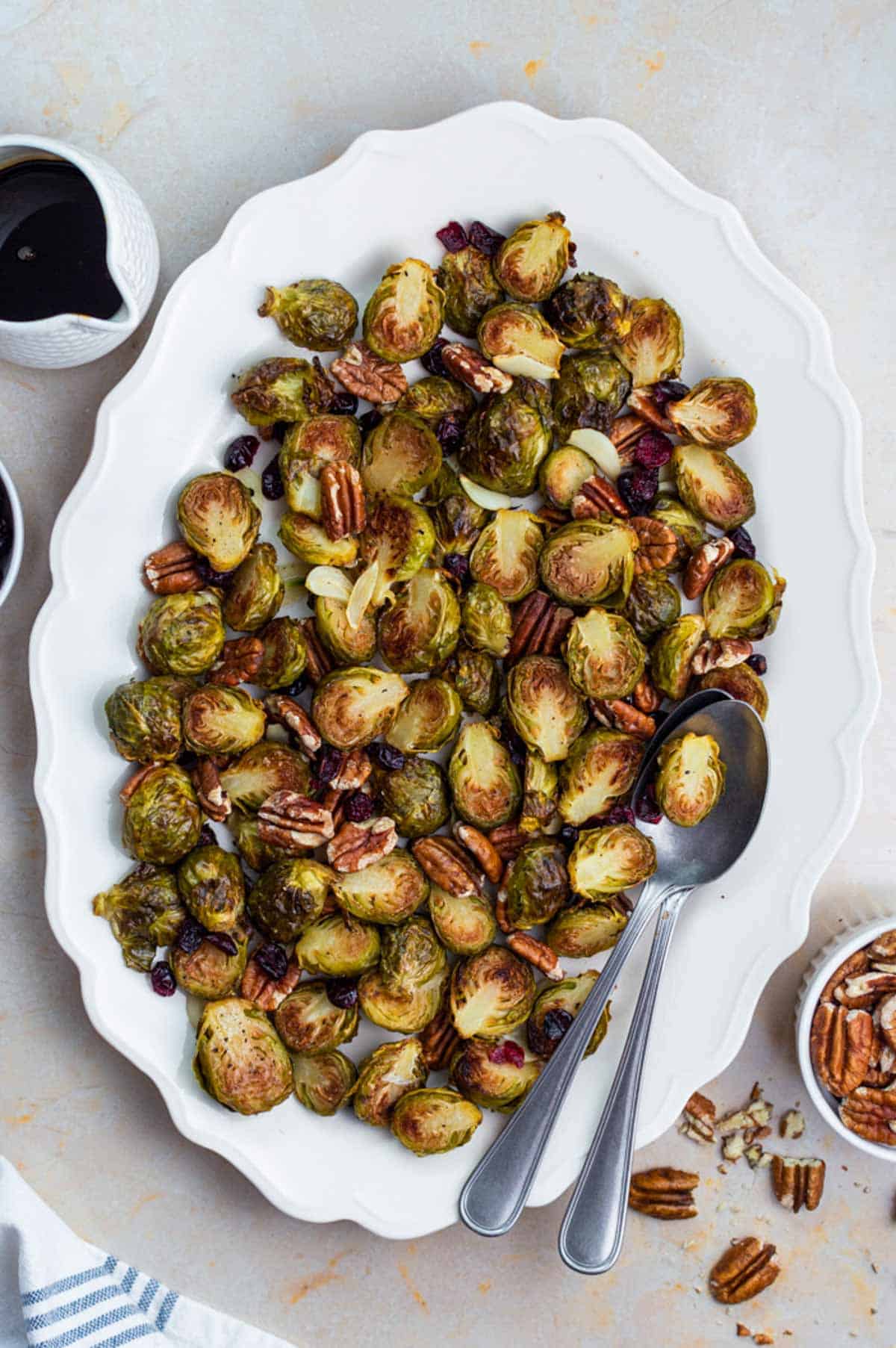 A white plate filled with frozen roasted Brussels sprouts. Two stacked silver spoons placed on the plate.