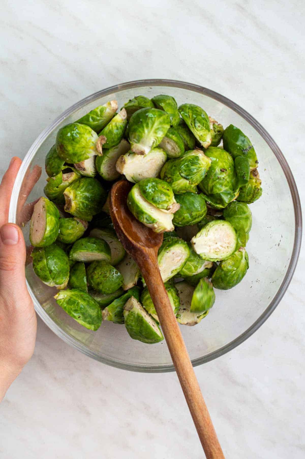 Tossing halved frozen Brussels sprouts with oil and spices in a mixing bowl.