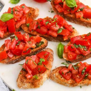 Tomato bruschetta on a white plate topped with fresh basil.