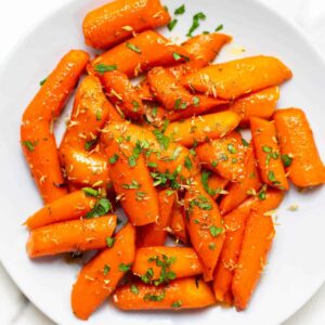 Glazed carrots on a white plate, topped with chopped parsley.