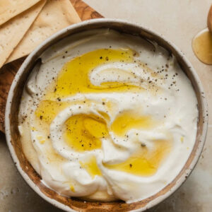 Whipped ricotta dip in a white bowl, topped with a drizzle of olive oil and cracked black pepper.