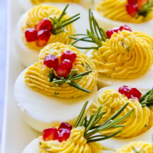 Deviled eggs on a white plate topped with pomegranate seeds and rosemary.