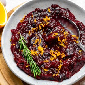 Cranberry sauce made from dried cranberries served in a white bowl and topped with orange zest and fresh rosemary.