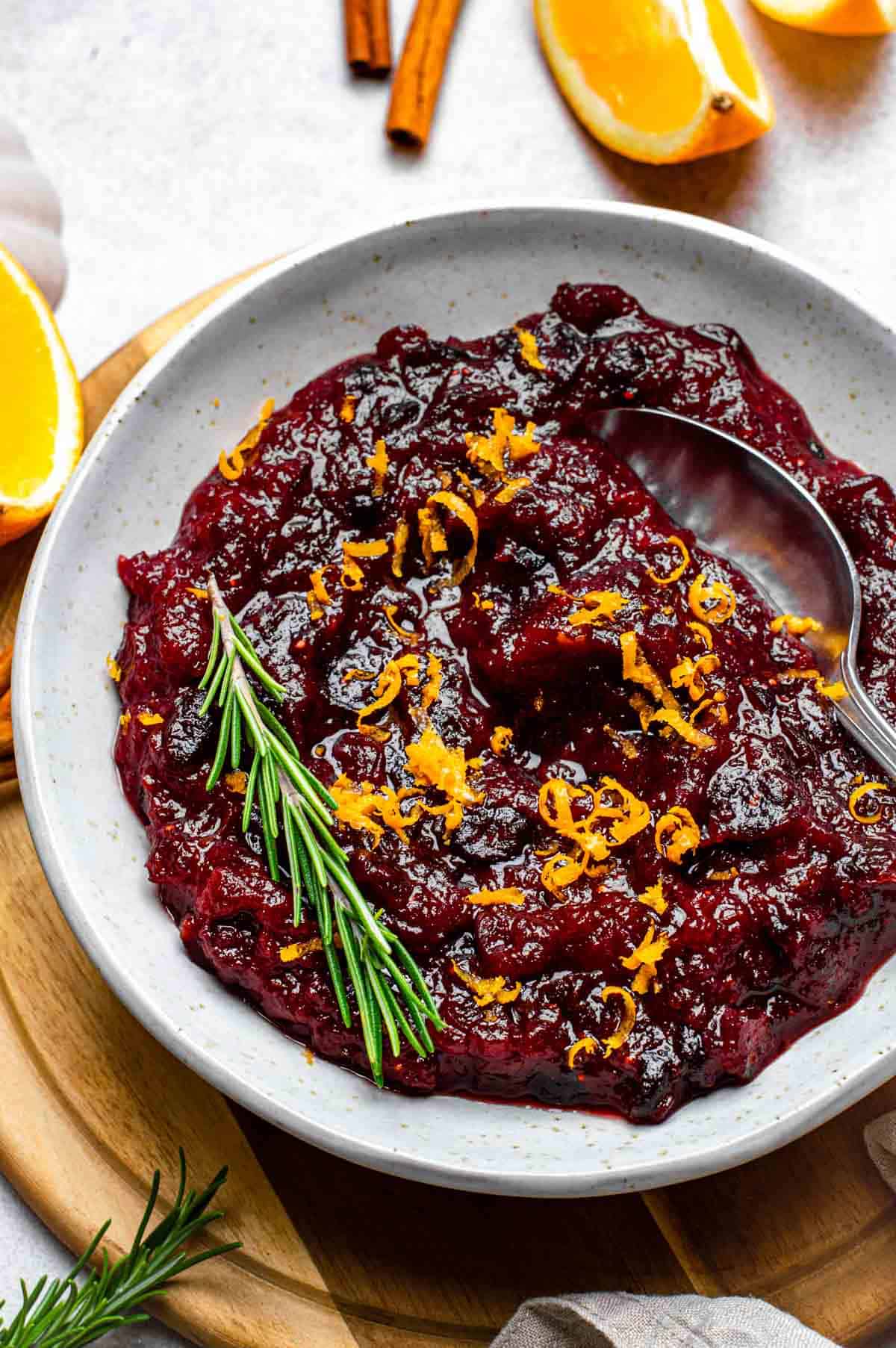 Cranberry sauce made from dried cranberries served in a white bowl and topped with orange zest and fresh rosemary.