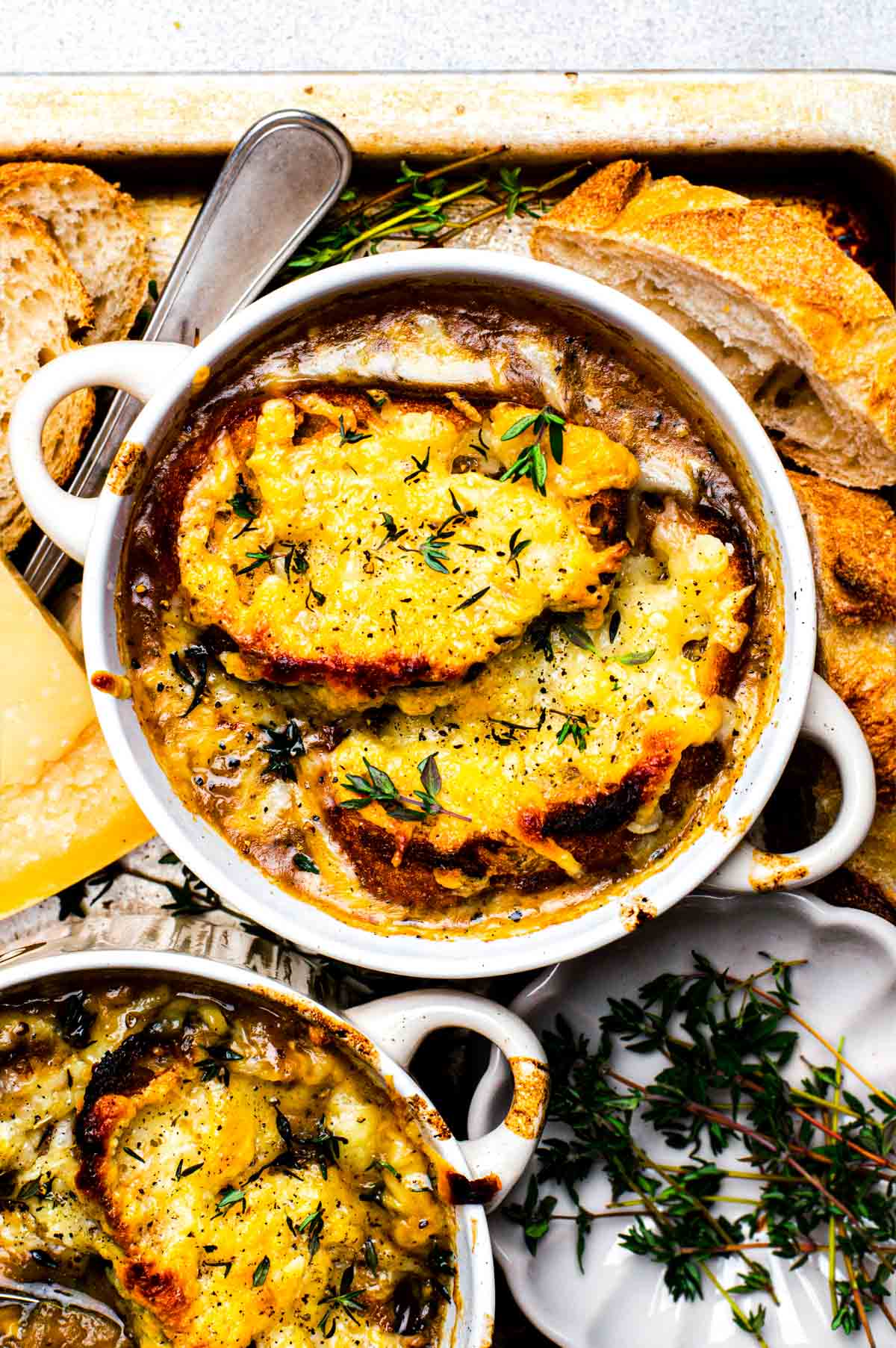 A white bowl filled with French onion soup topped with cheesy baguettes and fresh thyme
