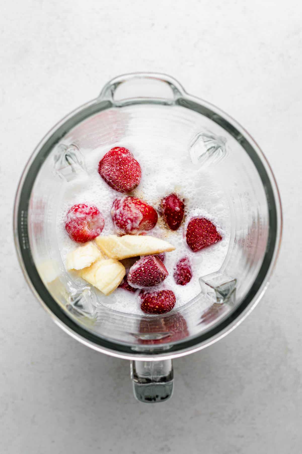 A blender filled with coconut milk, strawberries, bananas, and vanilla extract.