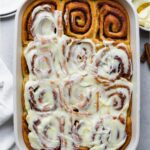 Cinnamon rolls in a ceramic baking dish covered with icing without cream cheese.