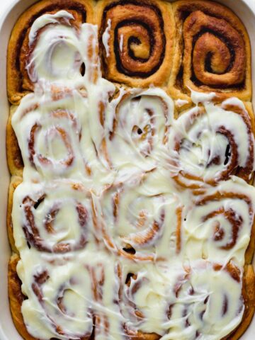 Cinnamon rolls in a ceramic baking dish covered with icing without cream cheese.