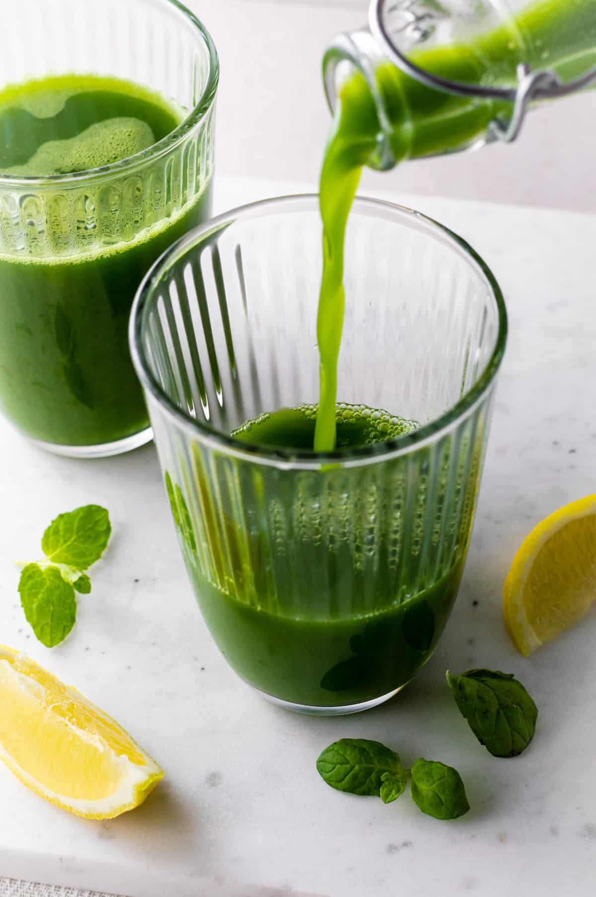 Pouring kale tonic into a large cup from a glass bottle.