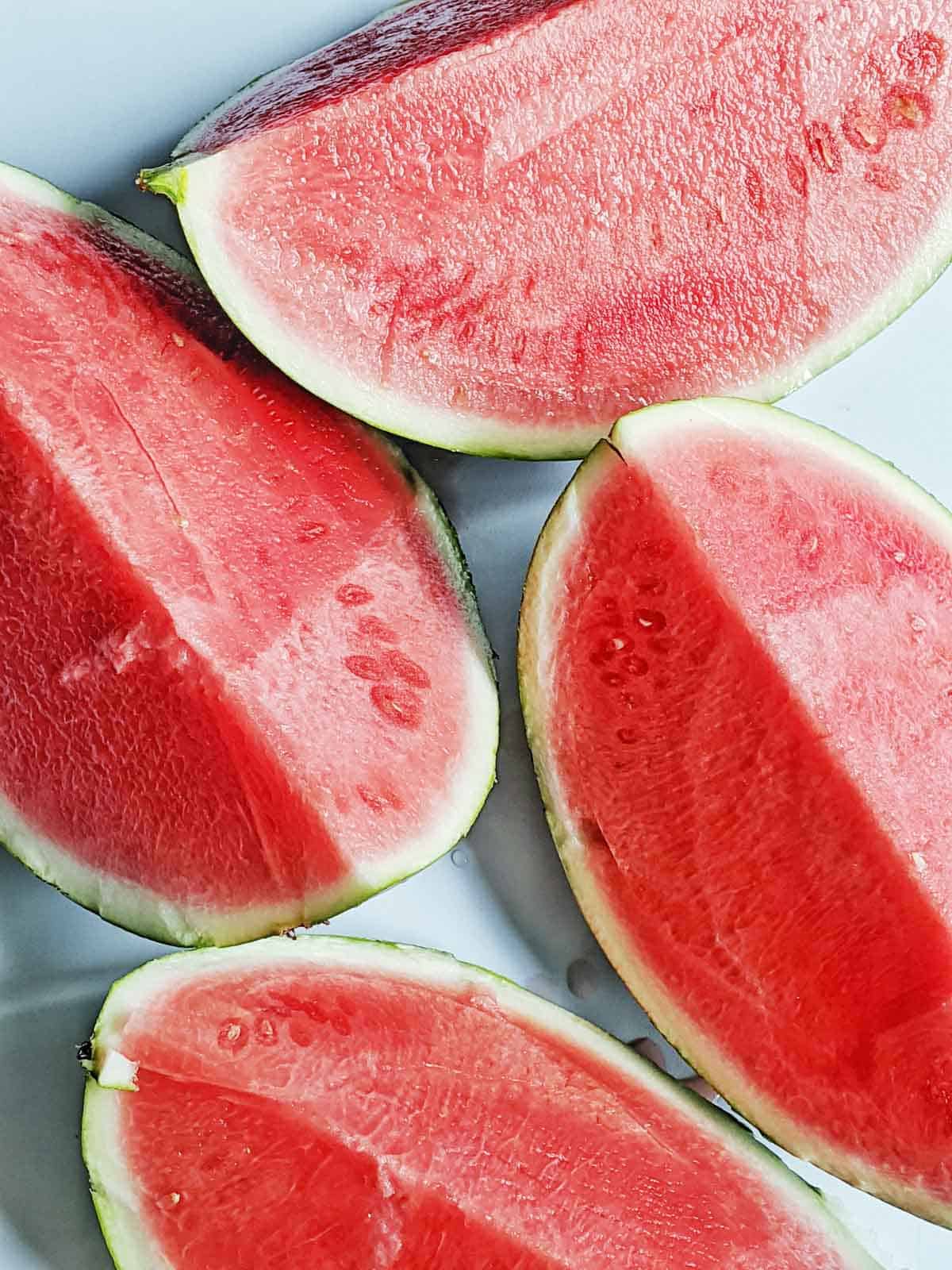 Four pieces of watermelon on a white countertop.