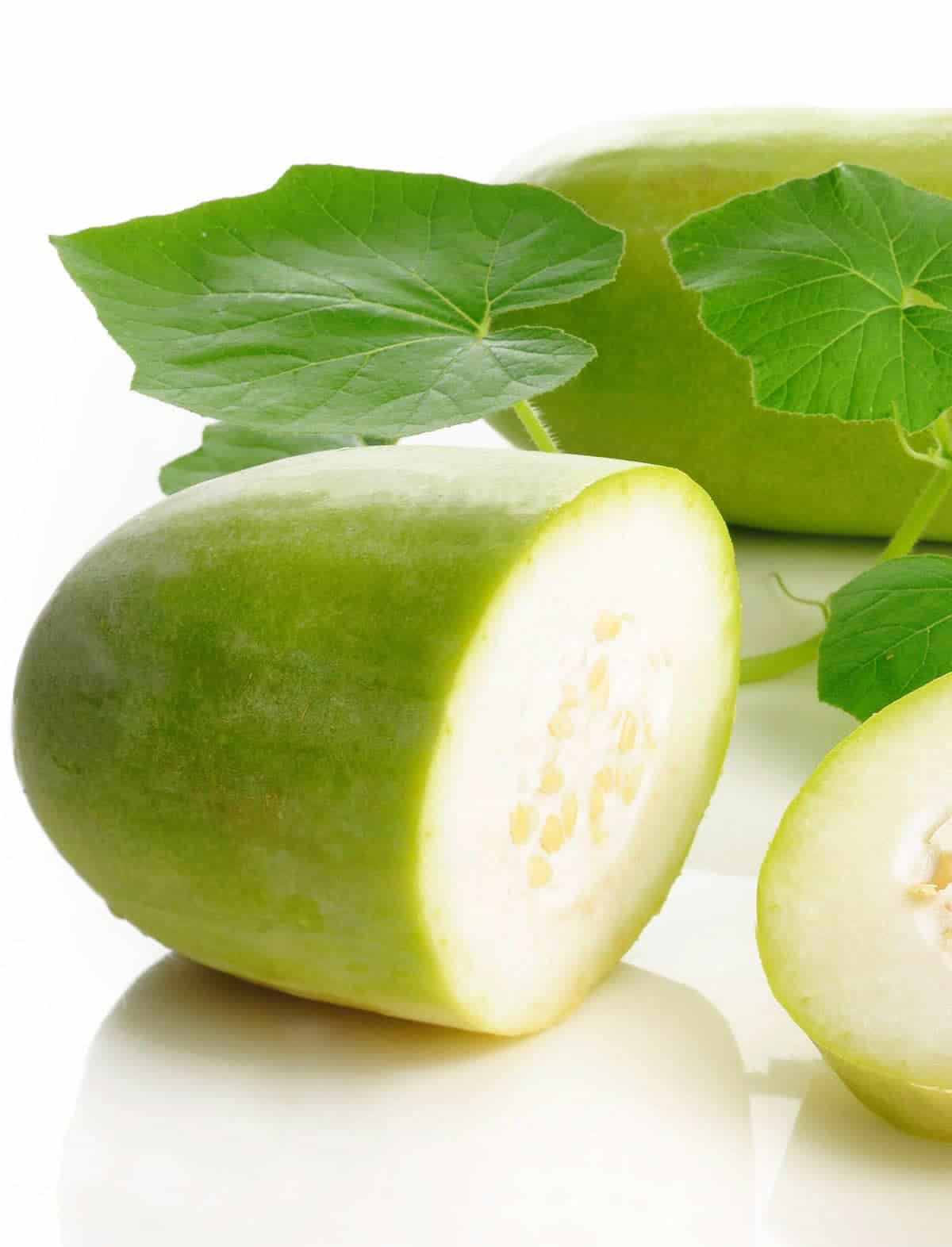 A halved winter melon on a white background with a snob of green leaves behind it.