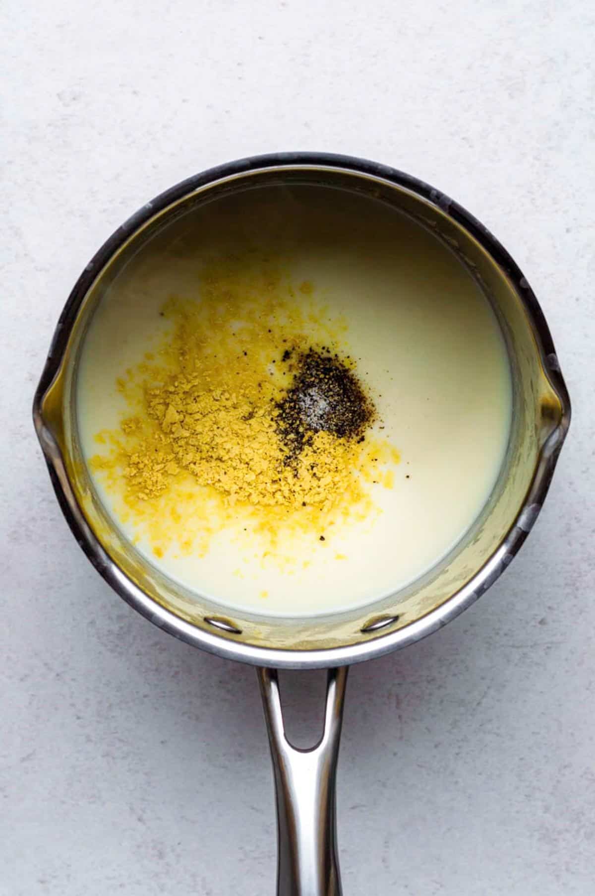 A saucepan filled with vegan white sauce seasoned with nutritional yeast, black pepper, and salt.