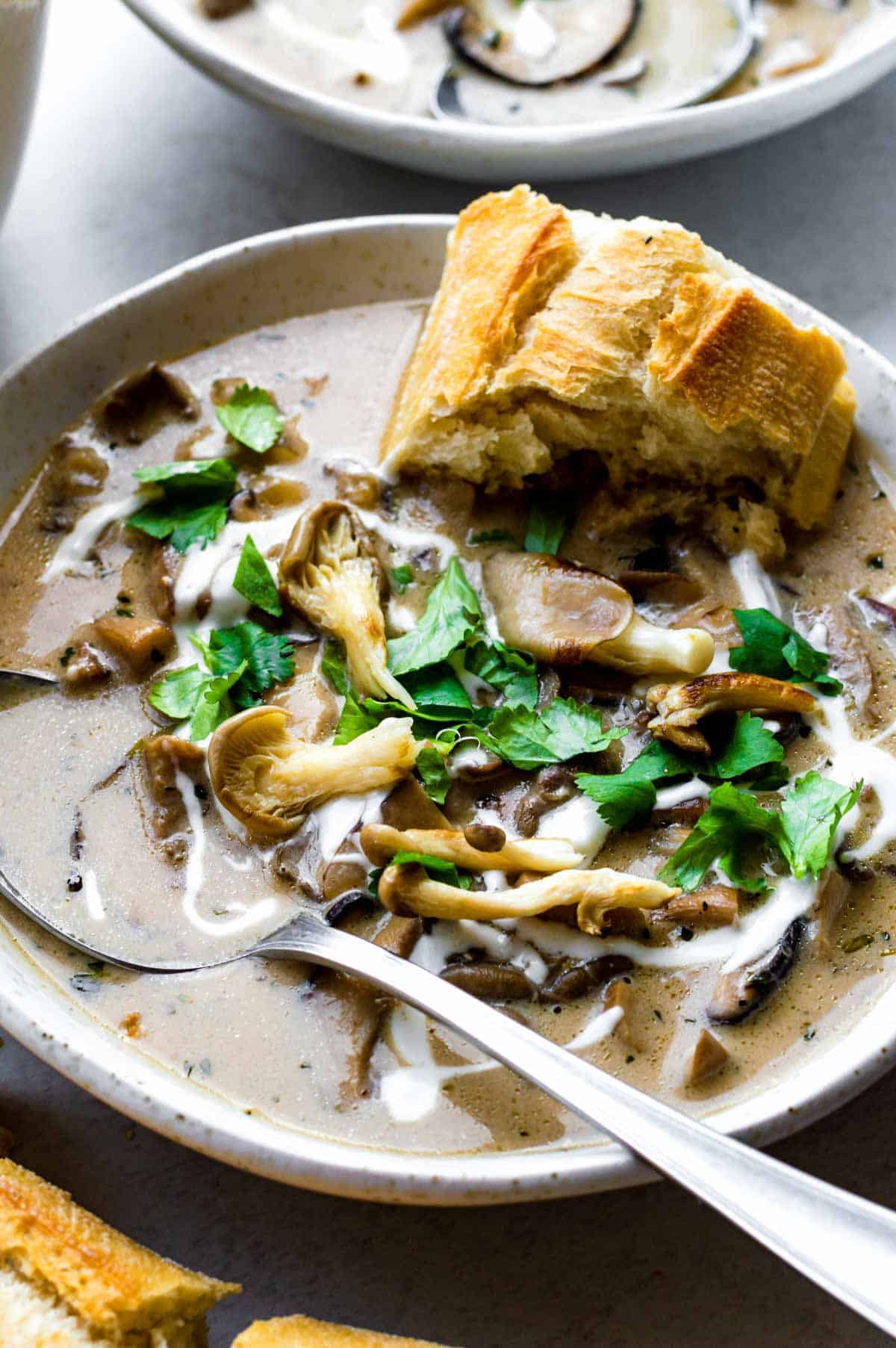 A white bowl filled with vegan oyster mushroom soup and served with fresh bread.