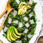 Spinach arugula salad served in a white platter and topped with avocado, parmesan and sunflower seeds.