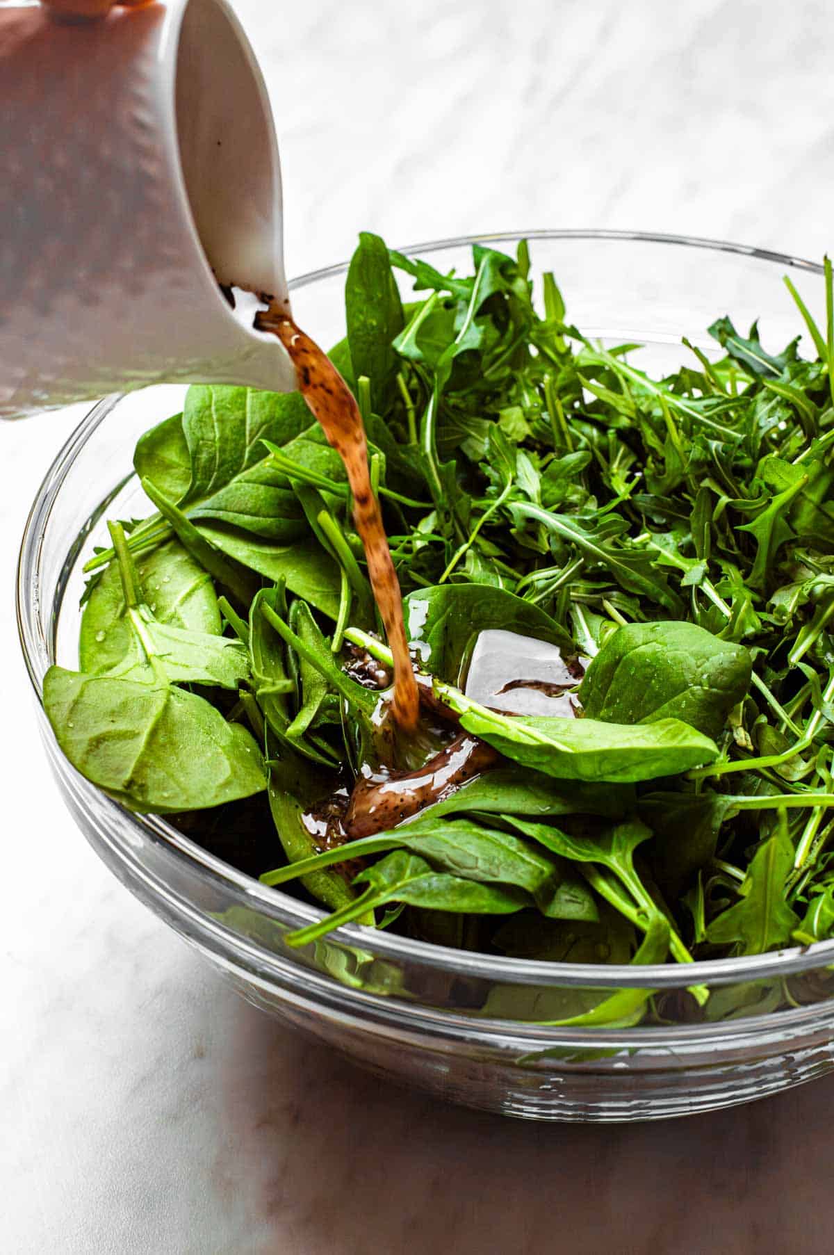 Pouring sumac dressing over agreens in a large bowl.