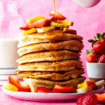 Pouring maple syrup onto a stack of vegan Bisquick pancakes.
