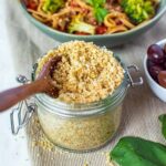 Vegan parmesan cheese served in a glass jar with a wooden spoon in it.