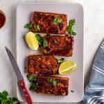 Vegan tofu ham on a pink platter, served with fresh parsley and lime wedges.